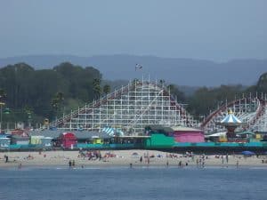 The white wooden Giant Dipper coaster rising behind the painted arcades of Santa Cruz Beach Boardwalk, seen from the water