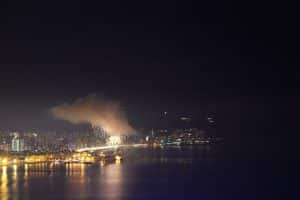 Fireworks bursting over the sea in front of Benidorm's lit seafront at night, seen from across the bay