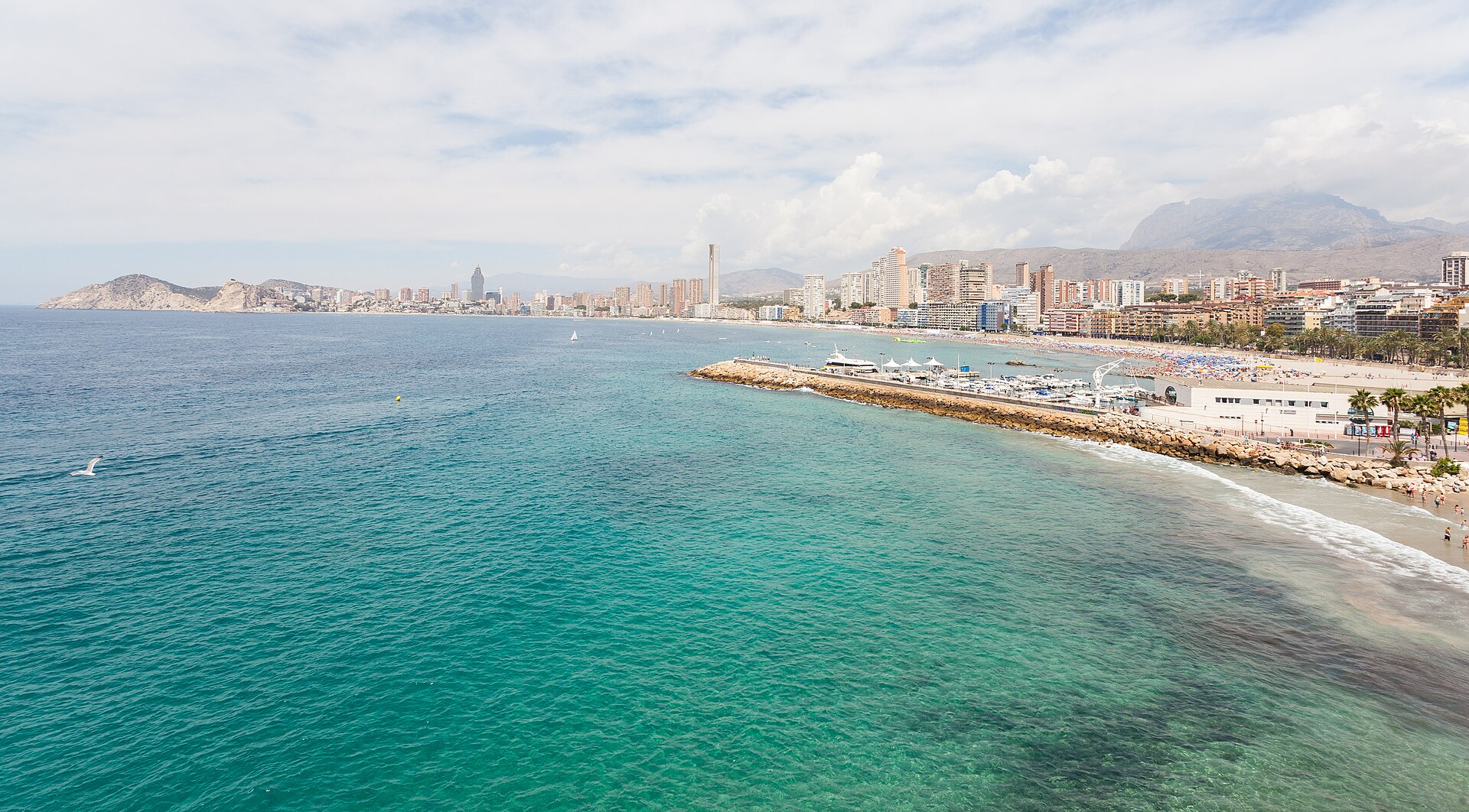 Playa de Poniente in Benidorm seen from the harbour breakwater, with the beach, promenade and mountains behind