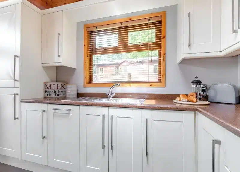 a kitchen with white cabinets and a window at Charlesworth Lodges in Glossop