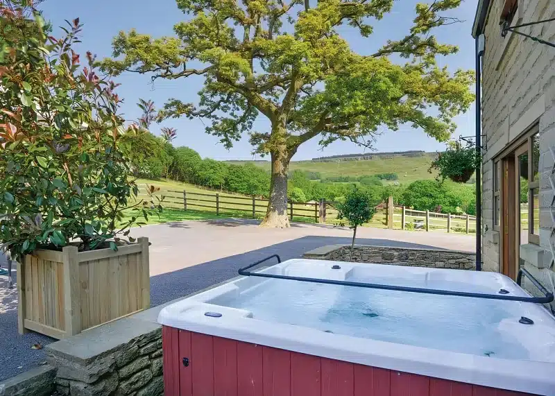 A hot tub on a terrace beside a stone building, with fields and a ridge beyond.