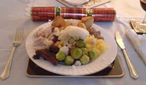 A Christmas dinner of roast turkey, Brussels sprouts, roast potatoes and chipolatas on a laid table beside a Christmas cracker