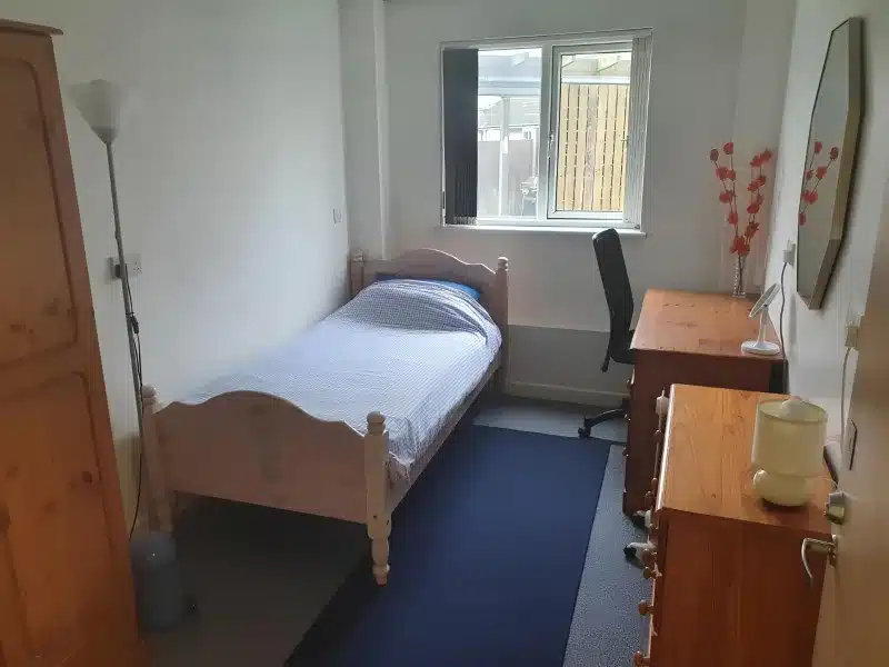 A single bedroom with a pale wooden bed, blue checked bedding, a desk and a chair.
