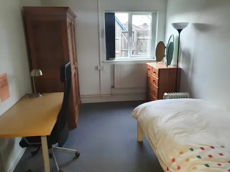 A single bedroom with a bed, a wooden wardrobe, a desk and an office chair.