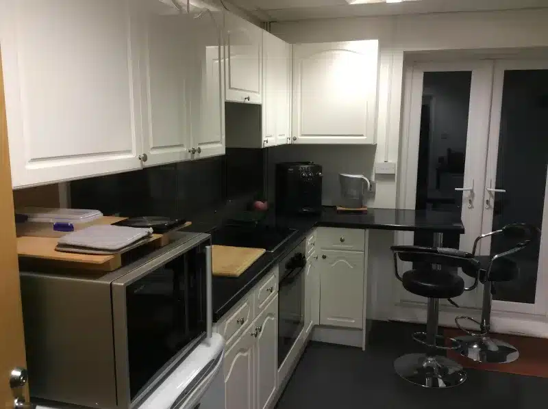A shared kitchen with white cabinets, a hob, oven, microwave and two stools.
