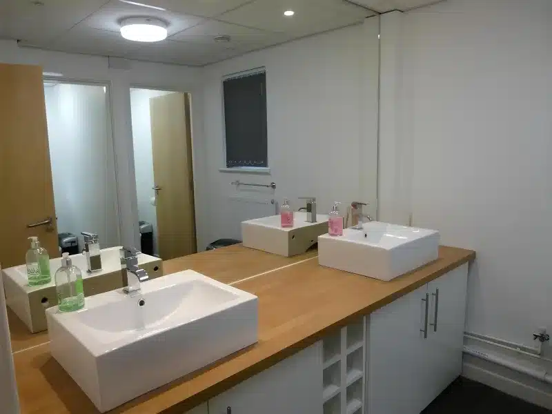 A shared washroom with three basins along a wooden counter.