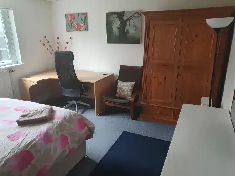 A double bedroom with floral bedding, a desk, an armchair and a pine wardrobe.
