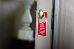 A red Do Not Disturb sign hanging from a brass door knob on a hotel room door