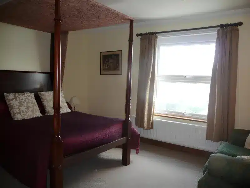 Four-poster double bed with burgundy cover in the larger lake-view double
