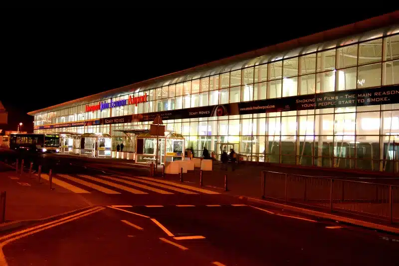 Liverpool John Lennon Airport at night: the glass terminal front, a bus at the stop, and the road in front.