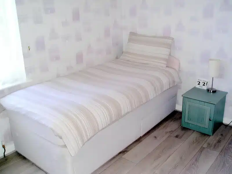 A single bed with a striped cover and a small green bedside cabinet in a room at Liverpool Airport Rooms.