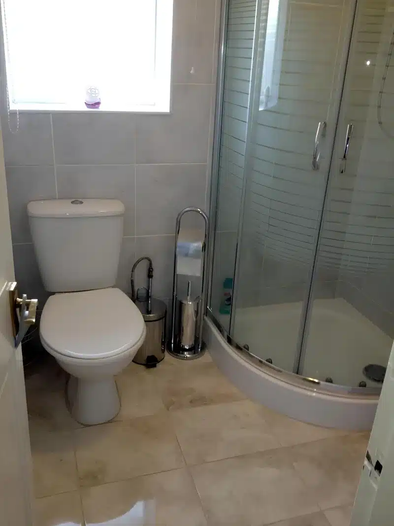 A shower over a bath, a toilet and a window in the bathroom at Liverpool Airport Rooms.