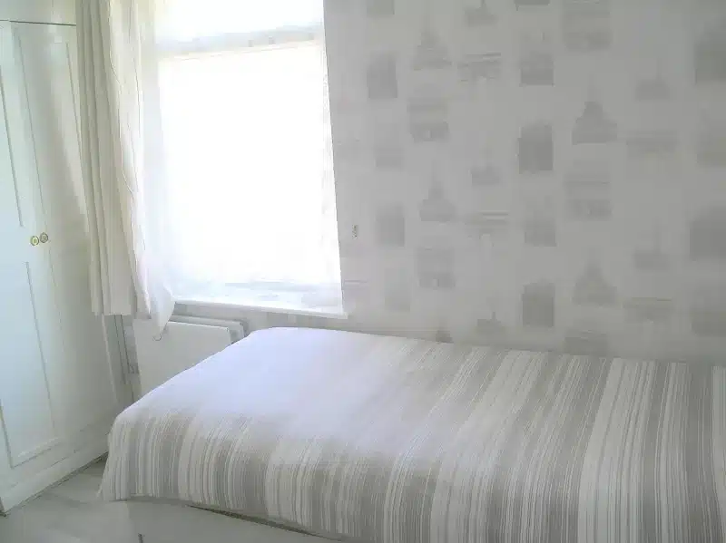 A single bed beside a bright window and a white wardrobe at Liverpool Airport Rooms.