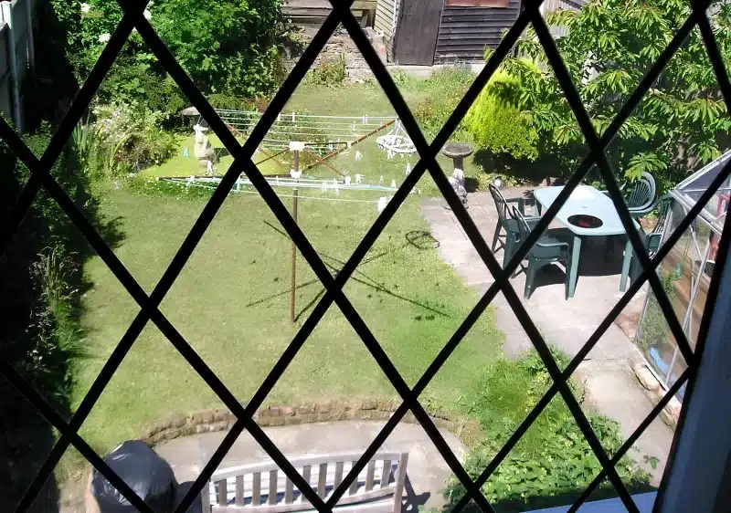 The back garden at Liverpool Airport Rooms, seen through a leaded window: lawn, rotary dryer and a patio table.