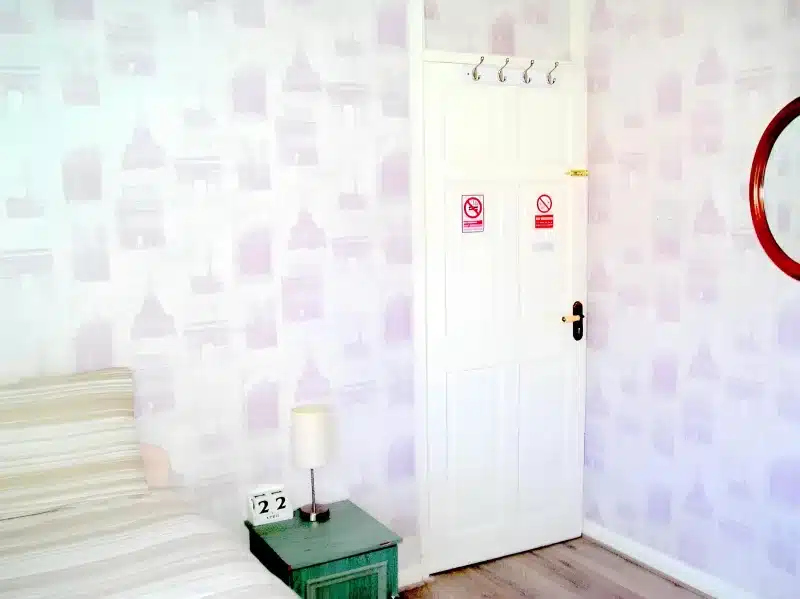 The room door, with coat hooks, beside the single bed at Liverpool Airport Rooms.