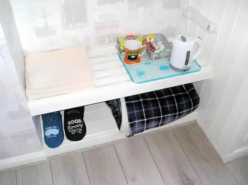 A kettle, tea, towels and slippers on a shelf in the room at Liverpool Airport Rooms.