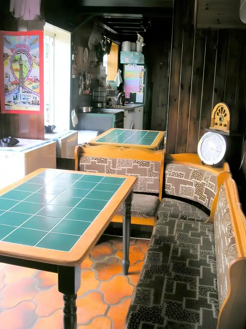 Green tiled tables and wooden benches, with the kitchen through the doorway, at Liverpool Airport Rooms.