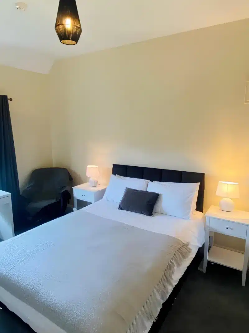 A double bed with white linen, a grey throw and a dark headboard in a cream bedroom.