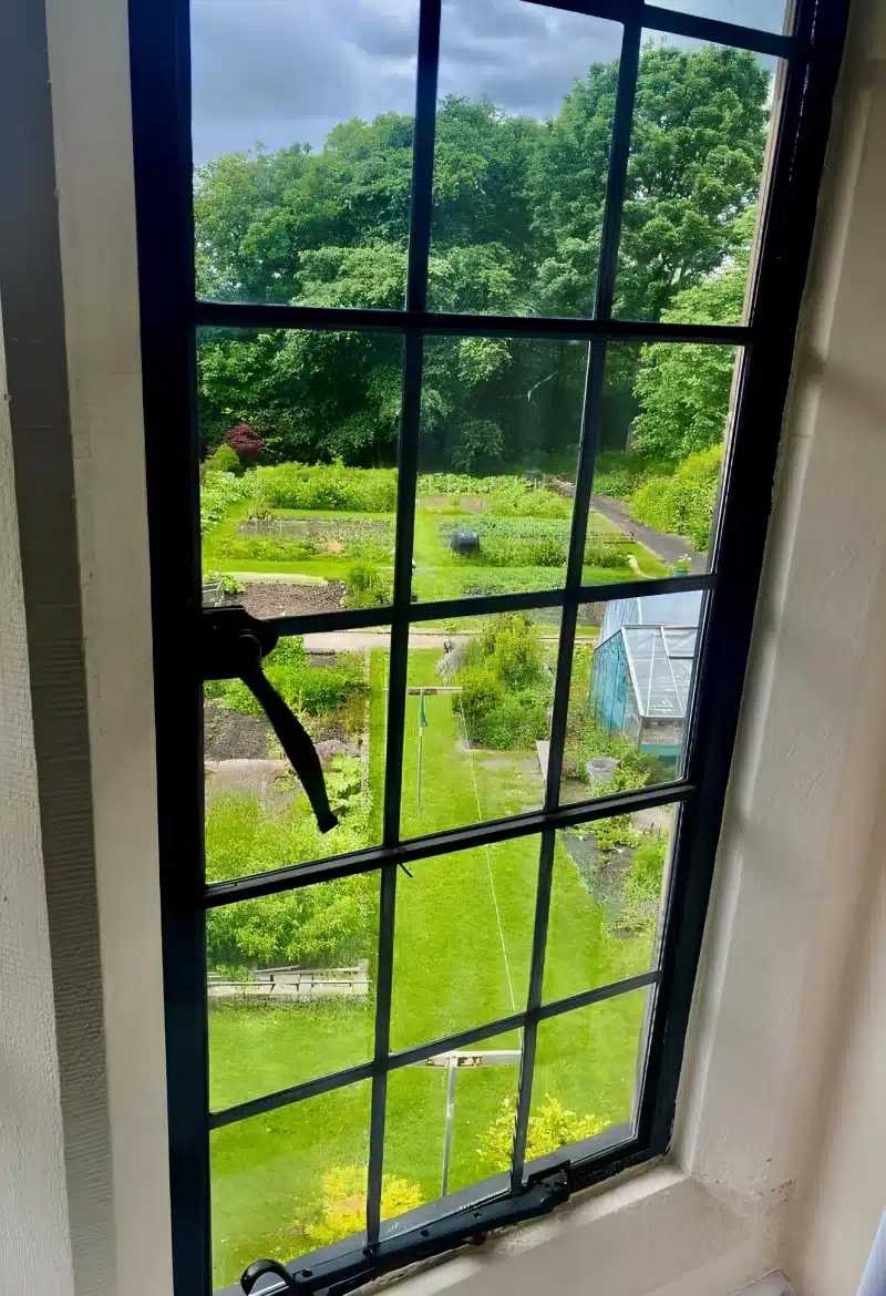 A leaded window looking over a lawn, vegetable beds and a greenhouse.