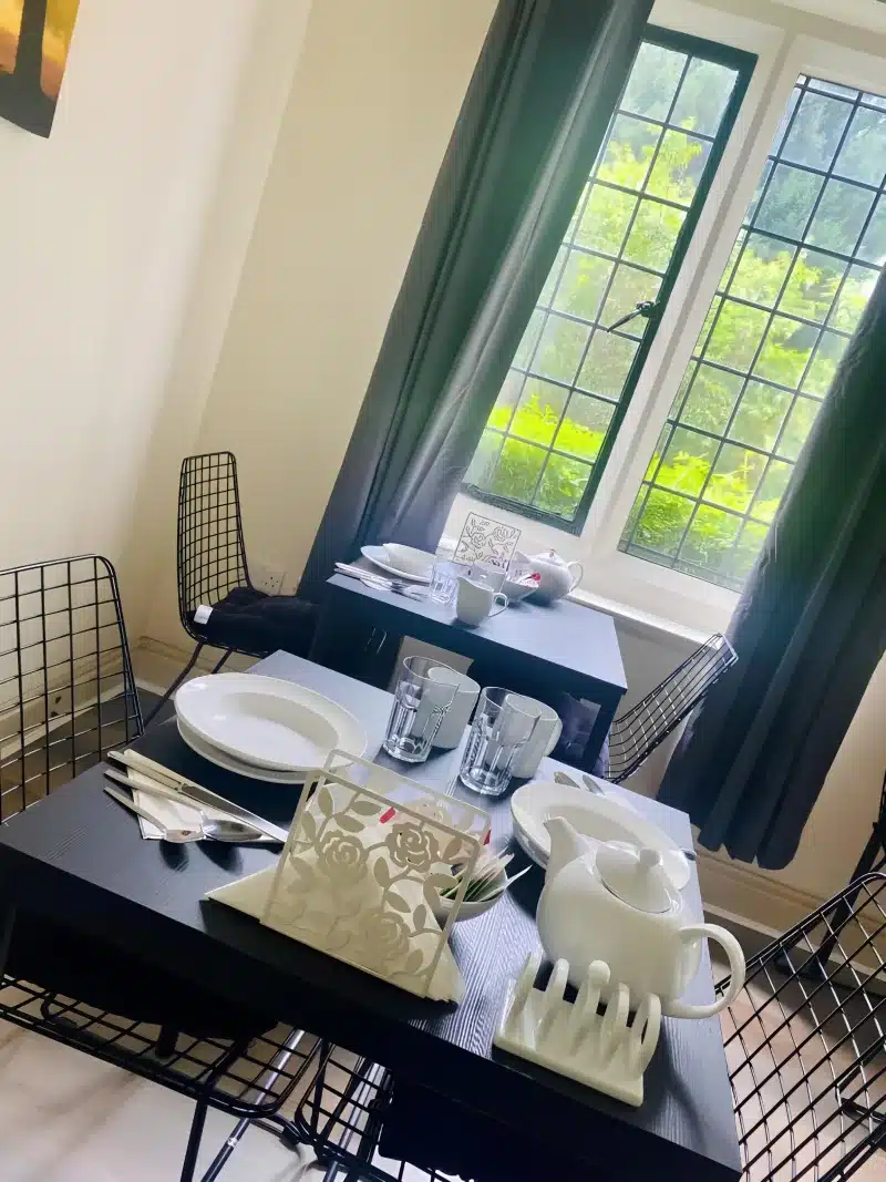Tables set with white plates, teapots and glasses beside a window onto the garden.