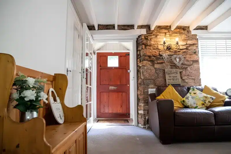 A sitting room with a brown leather sofa, yellow cushions, a stone wall and a wooden settle.
