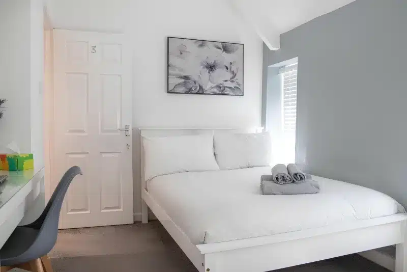 A white double bed in a room with a door marked 3, and the edge of a desk and chair.