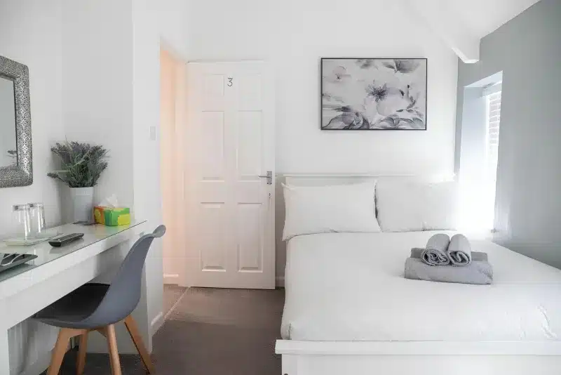 A white double bed, a door marked 3, and a glass desk with a grey chair.