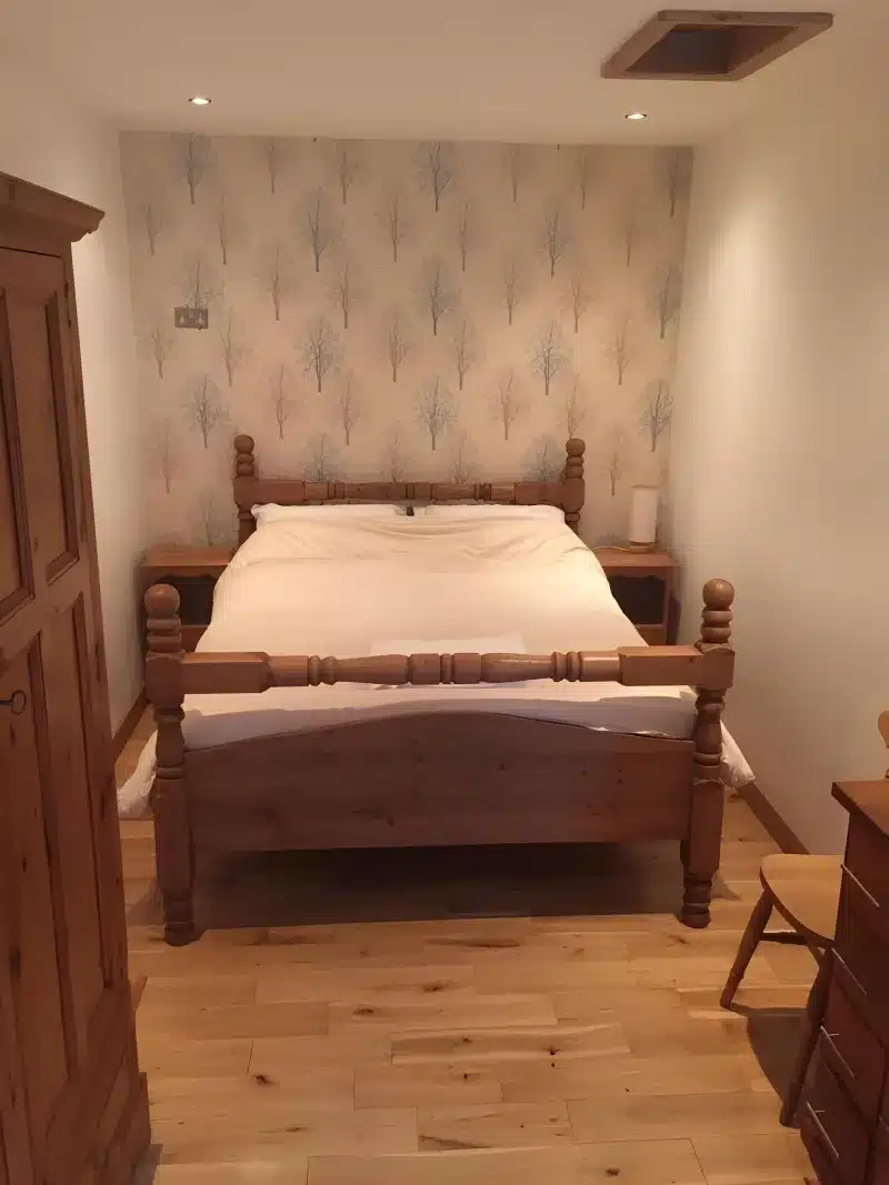The bedroom from the doorway, with the wooden bed, wardrobe and tree wallpaper.