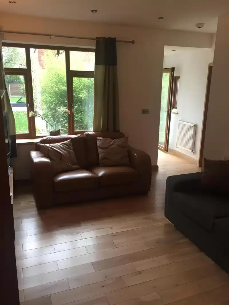 Sitting room with two sofas, a garden window and a door through to the hall.