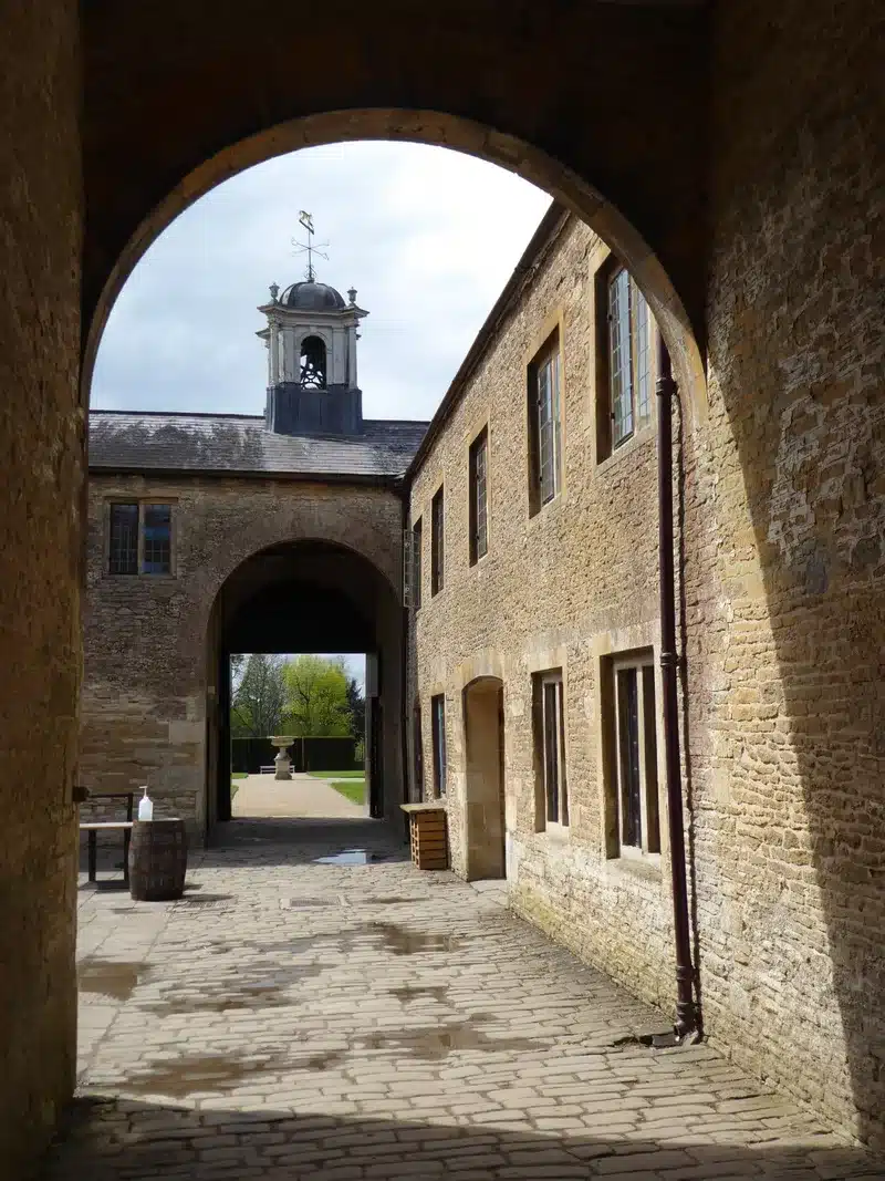 A stone courtyard at Dyrham Park, seen through an arch, with a cupola above the far range.