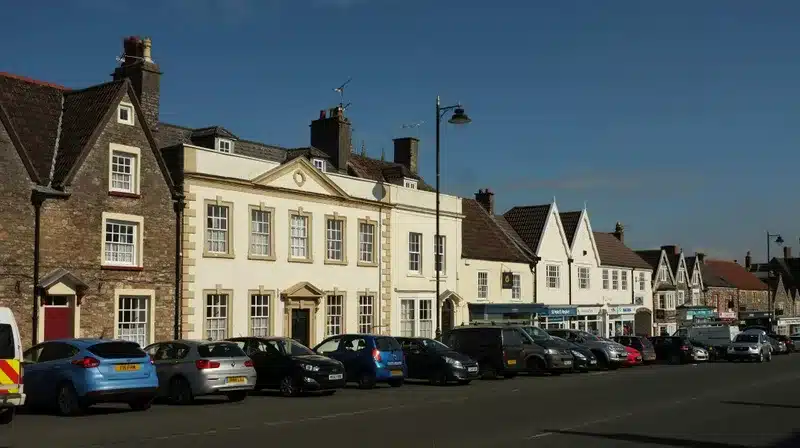 High Street in Chipping Sodbury, with stone and cream buildings and cars parked along the road.
