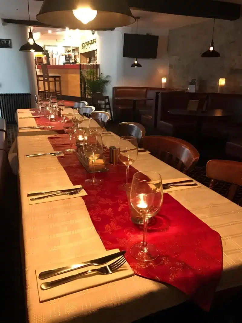 A long dining table with a red runner against a stone wall.