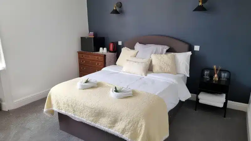 A double bed with a cream quilt against a navy wall.