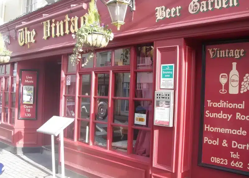 The red painted front of The Vintage Inn on Fore Street, with gold lettering, sash windows and a hanging basket.