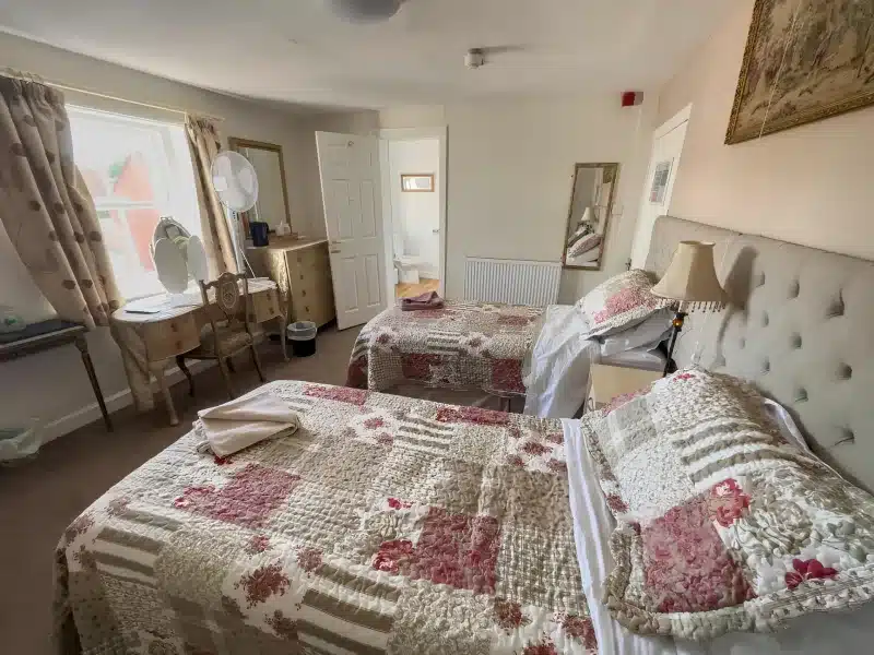 A guest bedroom with two single beds in floral quilts, and a bathroom visible through an open door.