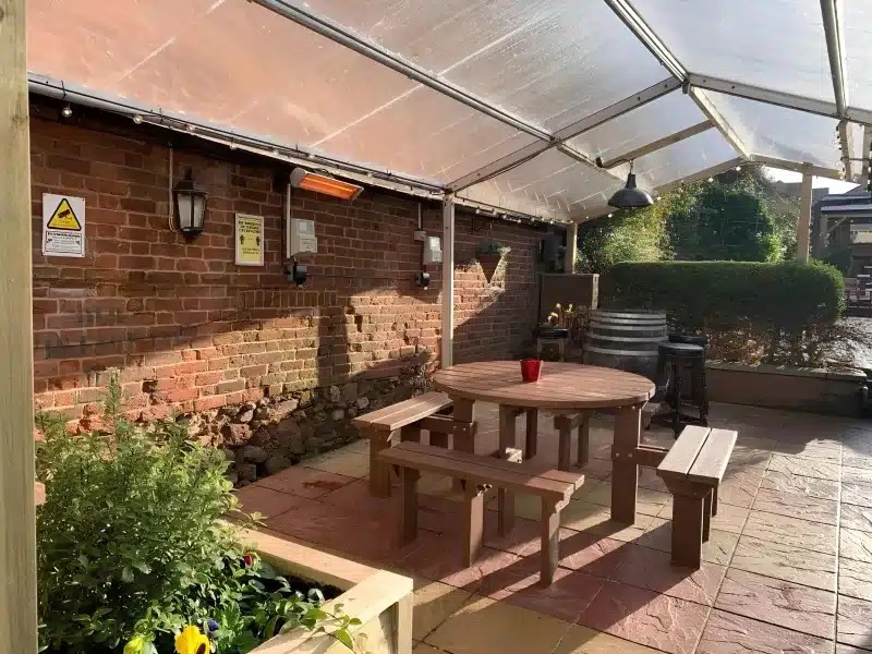 A covered table in the beer garden, with a patio heater and a brick wall.
