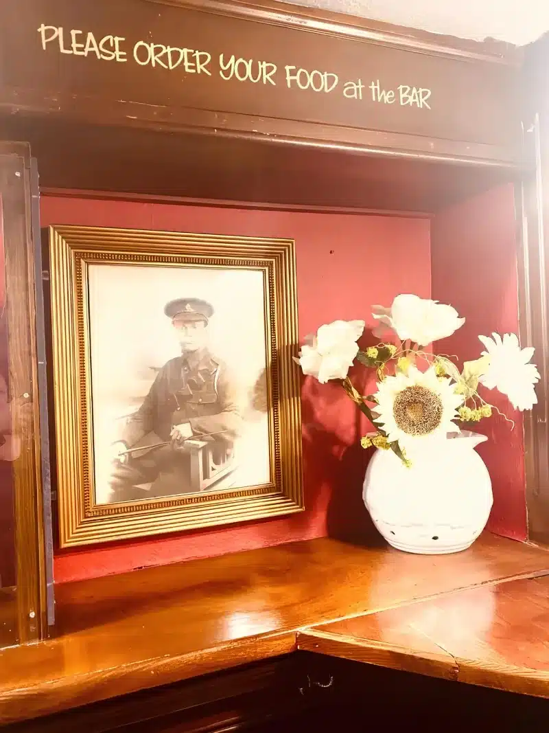 The bar interior, with a red wall, a framed portrait and a sign asking guests to order food at the bar.