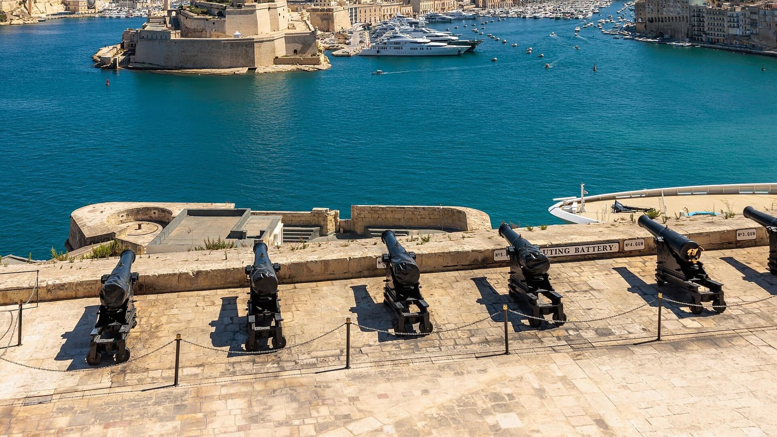 Cannons at the Saluting Battery overlooking Valletta's Grand Harbour, with Fort St Angelo and the Three Cities beyond.