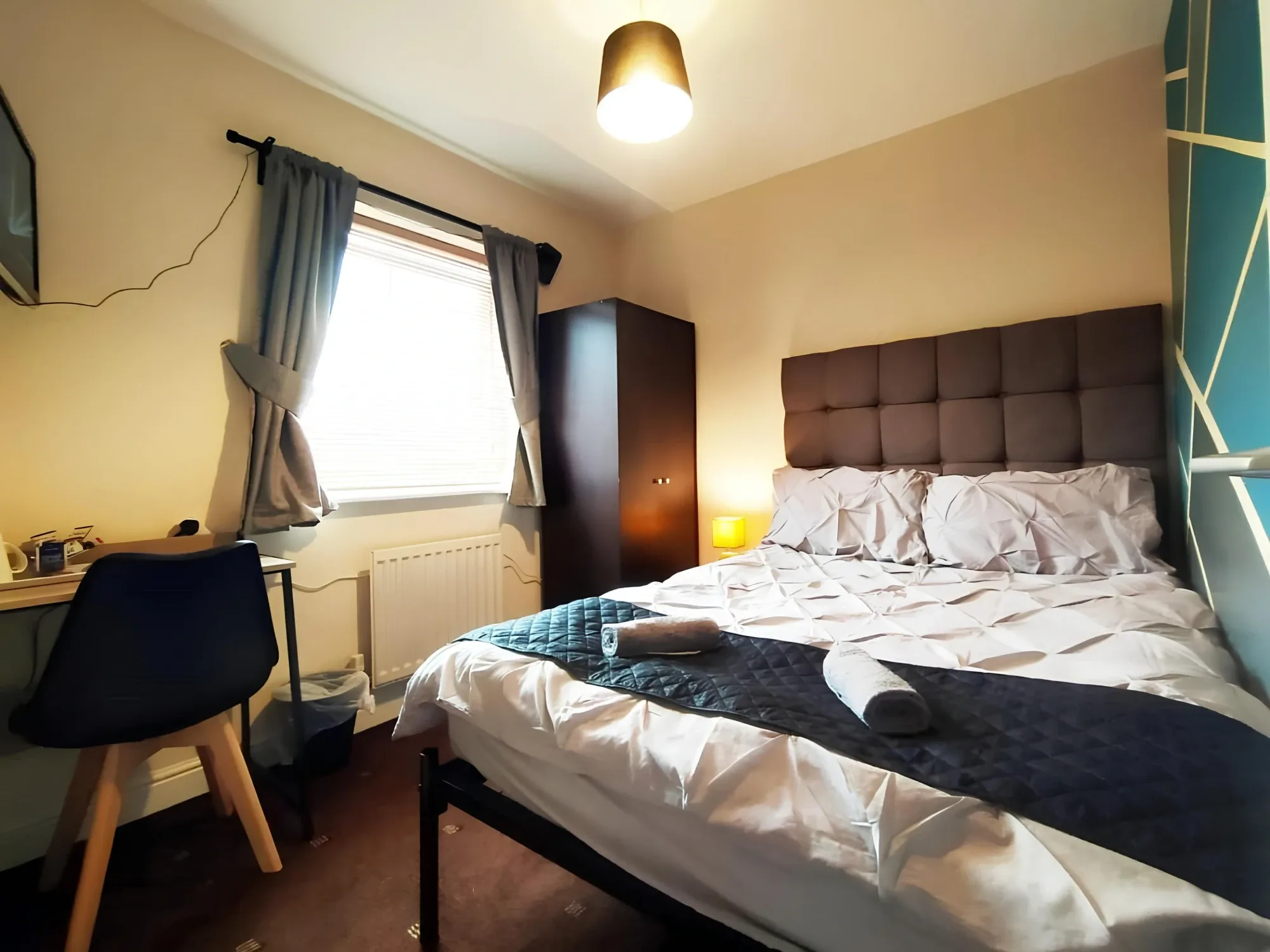 Bed, padded headboard and desk beside a window in a shared-bathroom double room