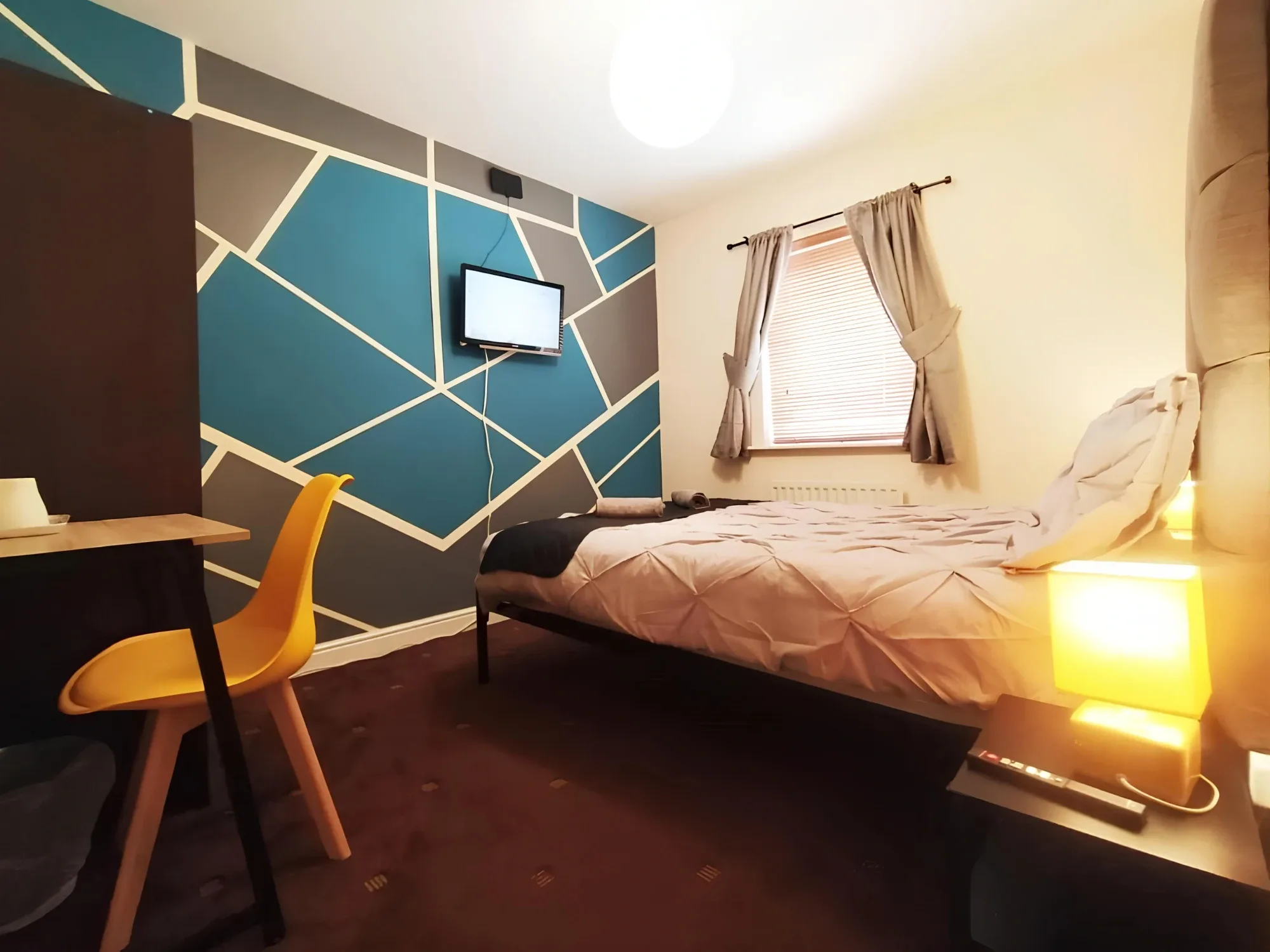 Bed, desk and teal geometric wall in a shared-bathroom double room at Bankwell Guest House