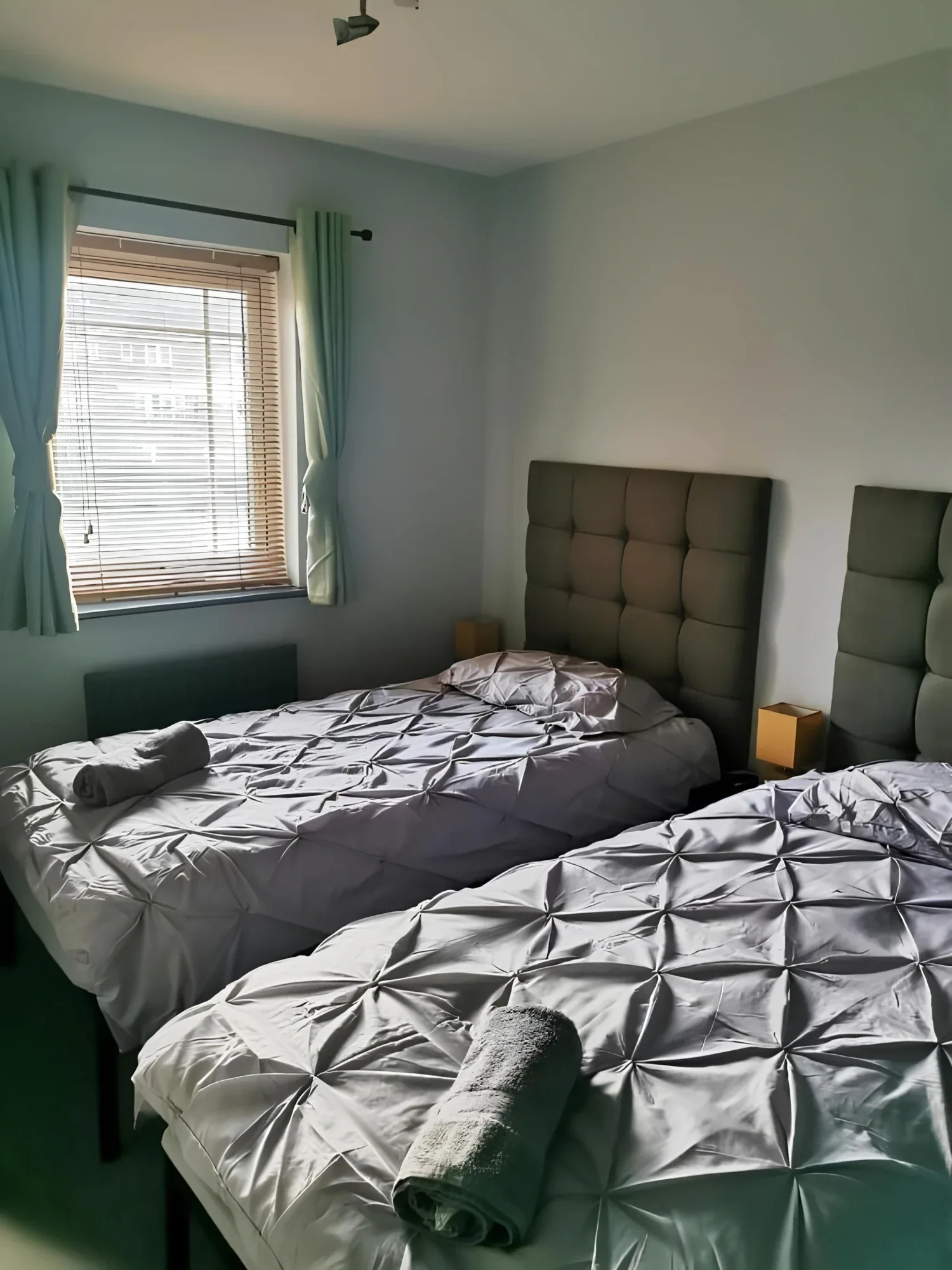 Two single beds beneath padded headboards beside a window in the Twin Room with Shared Bathroom