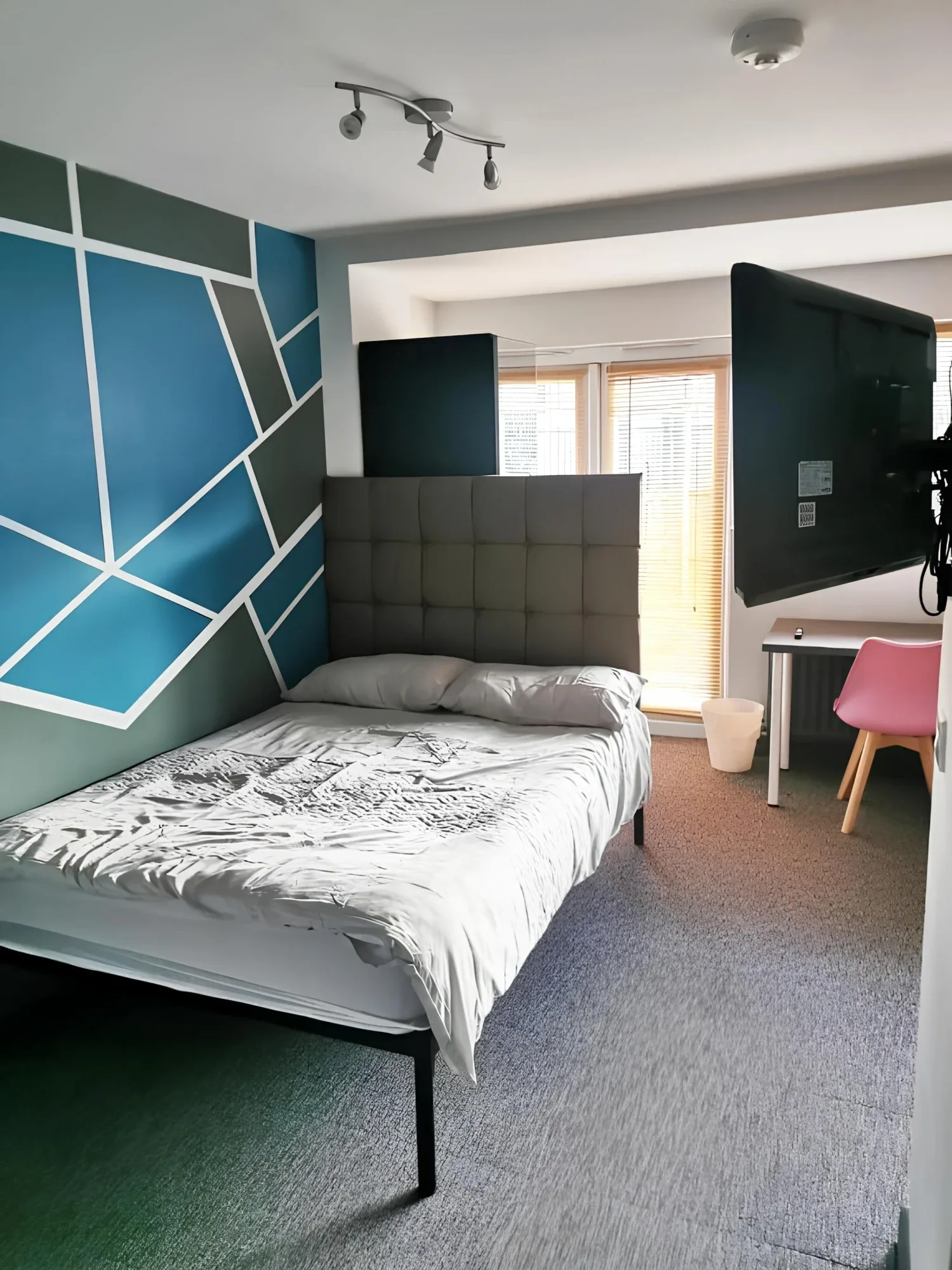 Double bed and television beside a teal geometric wall in the Studio
