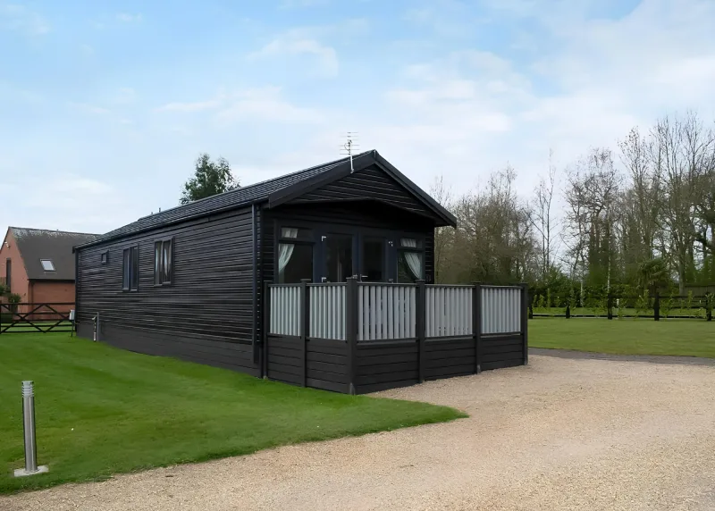 Dark timber lodge with covered deck beside grass